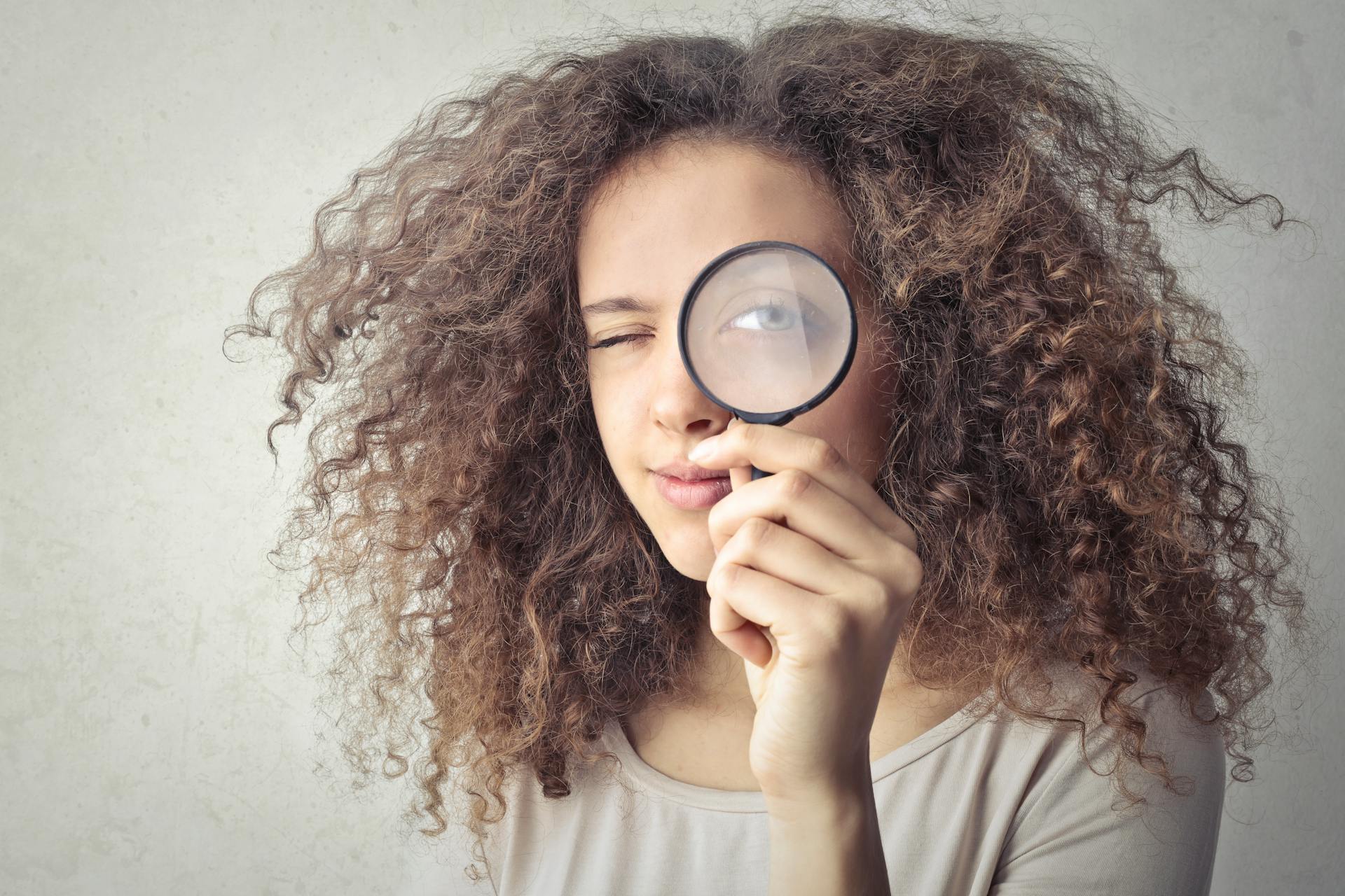 Une femme regarde à travers une loupe comme pour mener une introspection et apprendre à mieux se connaître.